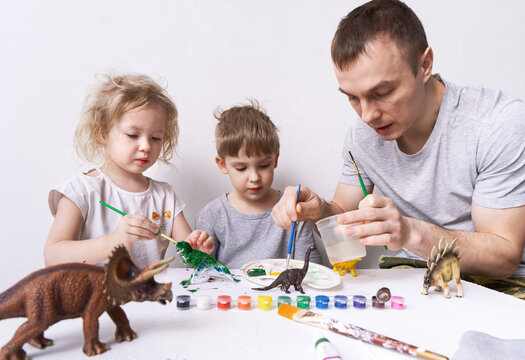 Hobby: dad with son and daughter paint small figures of dinosaurs with paint and a brush.