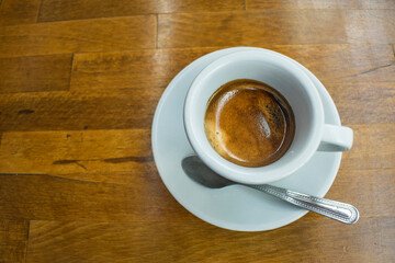 An aromatic cup of espresso coffee, on a saucer, shot from above on the wooden table.