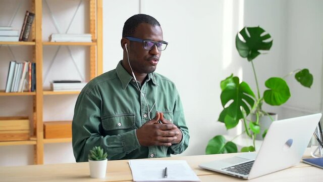 Millennial businessman discussing startup during online conference at table with laptop spbas. African American man talking with smile and looking at computer screen while sitting at desk in bright