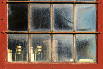 Closeup of a red window with old bottles with cork sealings behind a weathered glass