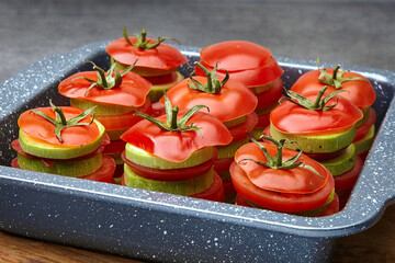 Sliced raw tomatoes and zucchini in a baking dish before roasting
