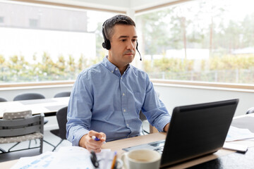 remote job, technology and business concept - middle-aged man with headset and laptop computer...