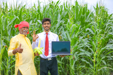 Indian farmer with agronomist at corn field and showing laptop screen