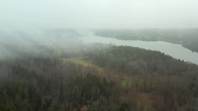 Fog or mist and low rain clouds over forest in aerial drone shot. autumn winter moody 4k view. lake with reflections in distant mysterious nature landscape
