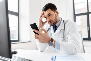 healthcare, medicine and people concept - male doctor with smartphone at hospital