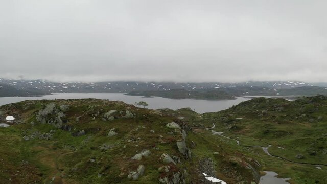 Norwegian mountain highland aerial drone view in 4k. Summer day rainy and cloudy. Granite rocks and lake with some snow. Low angle video over Norway stinted meager scant or sparse open landscape