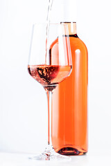 Rose wine pouring out of the bottle, white bakcground. Rosado, rosato or blush wine tasting in wineshop, bar concept. Copy Space