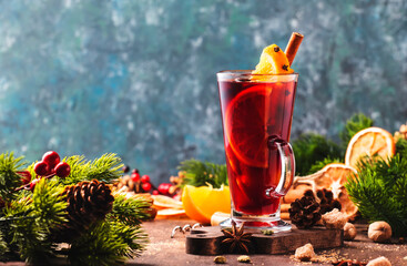 Christmas mulled red wine with spices and fruits in tall glass on wooden rustic table. Traditional...