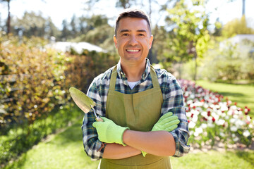 gardening and people concept - happy smiling middle-aged man in apron with trowel in crossed hands...