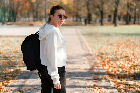 A young beautiful woman with a ponytail and sunglasses, with a backpack on his shoulders in the park. Photo from the back