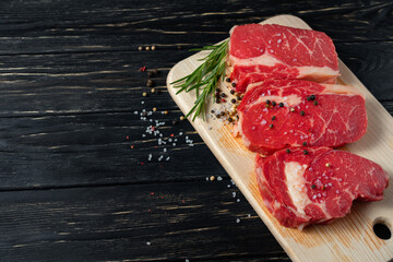 Three pieces of juicy raw beef on a cutting board on a black wooden table background.