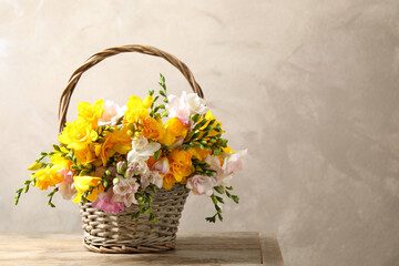 Beautiful blooming freesias in wicker basket on table against grey background. Space for text