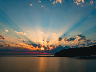 Beautiful, colorful sunset over the sea. Sun with rays at sunset under a cloudy sky.