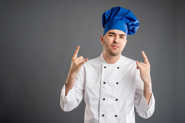 Young male dressed in a white chef suit doing rock symbol with hands up