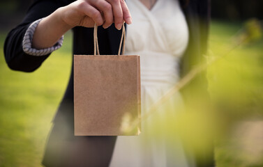 Woman in business outfit passing an small paper bag in a green outdoor situation