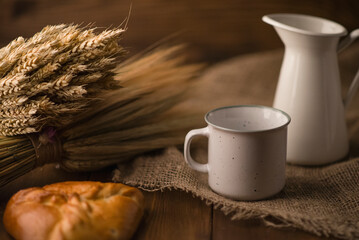 Enamel dishes on a wooden table with spikelets of cereals and bread in warm summer colors with a blurred background