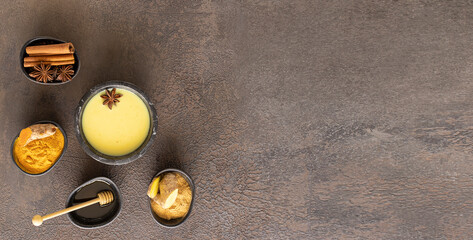 Ayurvedic Golden Milk beverage in black bowl with ingredients on large  background for banner. Alternative remedies for health and immune system