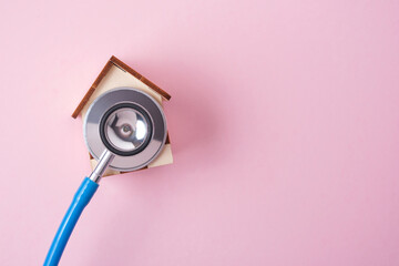 Fototapeta na wymiar Medical stethoscope and toy house on a pink background with copy space