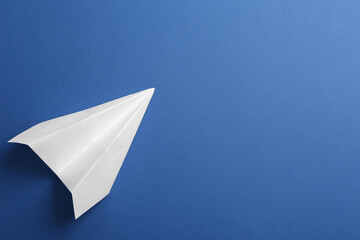 White paper plane on blue background, top view. Space for text