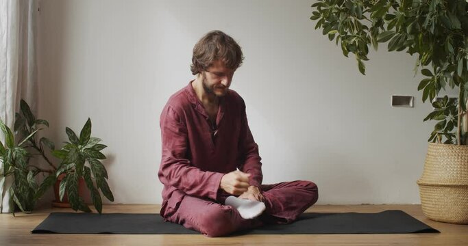 Professional thai masseur tapping foot on indoors tutorial slow motion. Man sitting on yoga mat massaging feet on master class natural light. Asian culture health body care. Special equipment fashion
