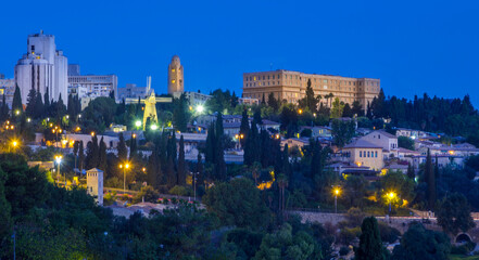 Fototapeta premium Blue hour at Mishkenot Shaananim and Yemin Moshe, first Jewish neighborhoods outside Jerusalem's Old City, with Montefiore Windmill, the YMCA tower and historic King David hotel on top of the hill