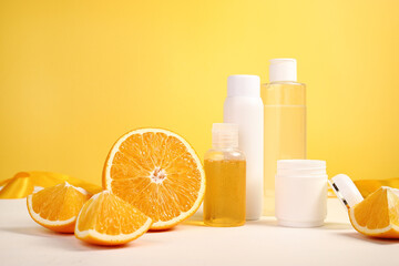 Shower gel, jar of cream, jars of cosmetics with oranges on a yellow background.