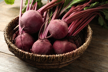 Raw ripe beets in wicker bowl on wooden table, closeup