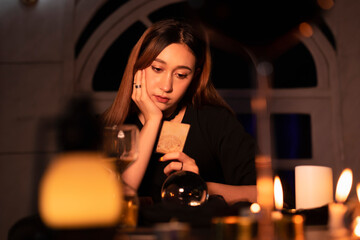 Beautiful young woman fortune teller using tarot card to predict the future in dark room.