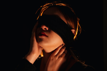 Blindfold beautiful woman isolate over black background.