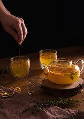 Sea buckthorn tea in a glass teapot, into which water is poured, there are mugs nearby