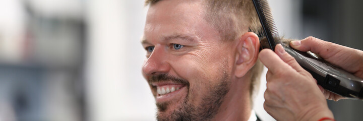 Obraz premium Master cuts man in beauty salon with machine. Services of hairdressing and beauty salons concept