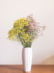Dried pink and yellow flowers in white vase against white wall. Home interior autumn decor