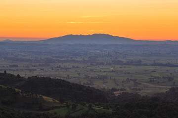 Fototapeta na wymiar A view over the Waikato Region, New Zealand, at sunset, taken from the Kaimai Mountains. On the horizon is Maungatautari, or Sanctuary Mountain