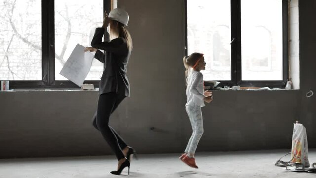 Mother builder architect engineer constractor dancing having fun with her little cute daughter indoors house. Concept of children and parent's work, break at work job 