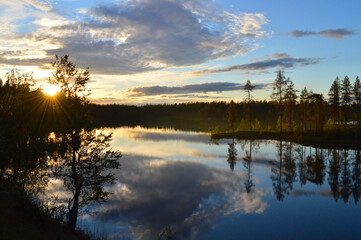 Naklejka na ściany i meble Late summers evening in Finland. Sunset on the lake, Haltiajärvi, Salla. Calm water, cloudlets in the sky, the last rays of the setting sun.