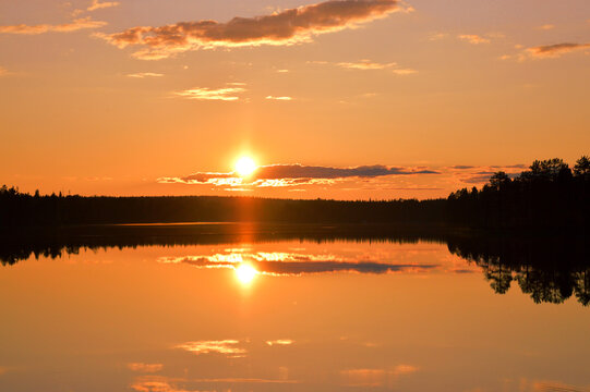 Sunset with strong colors. Lake, horizon, orange sky with cloudlets, glowing sun and reflection. Kemijärvi Finland.