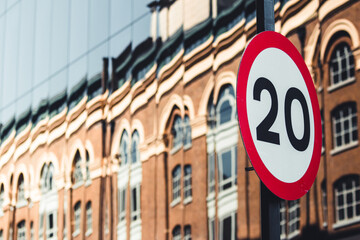 Close up shot of speed limit sign in an urban environment. Blurred background with mirrored facade reflecting a classical building. Driving limitations, social rules, European laws. 