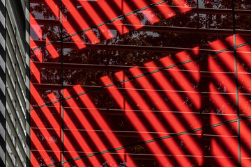 Public space defined by contemporary architecture, medium shot of shadow patterns dropping on red shiny walls, luxury details, steel and glass cladding, parallel geometric lines, new design features. 