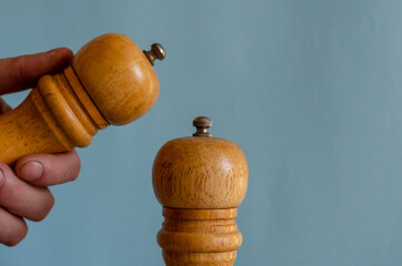Two peppermills and a hand on a blue background.