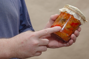 Male hands hold a glass jar of canned food.