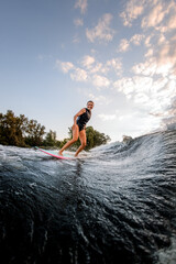 pretty young woman rides down on surf style wakeboard on splashed river wave