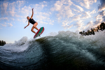 Young woman in swimsuit jumping up on surf style wakeboard against blue cloudy sky - Powered by Adobe