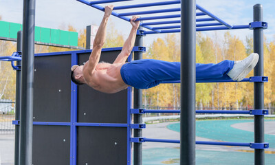 street workout. sporty man doing horisontal lever exercise. caucasian guy doing front lever on a street sportsground. outdoors active lifestyle. body building and fitness concept. 