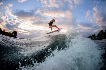 view of woman jumping over big splashing wave on surf style wakeboard.
