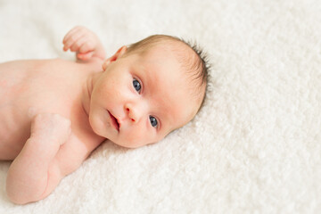 Cute naked newborn baby with open eyes, lying on a bed. A parent holds the legs of a newborn baby.