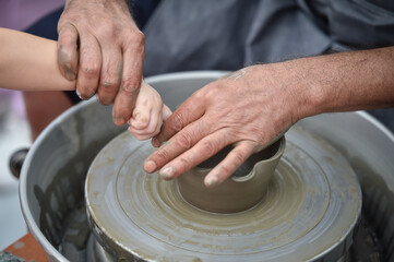 Detail with hands of an artist and hand of a child modeling a bowl on a pottery wheel