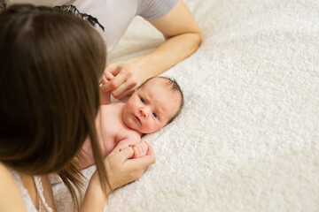 Cute naked newborn baby with open eyes, lying on a bed. A parent holds the legs of a newborn baby.