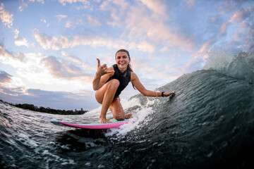 Fototapeta premium sportive woman on surf style wakeboard and rides the wave and show hand gesture