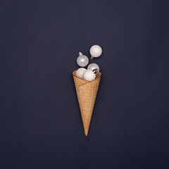 White glitter Christmas decoration baubles in ice cream cone on deep blue background. Creative concept for new year.