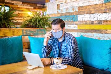 Young entrepreneur with protective face mask remote working in coffee shop